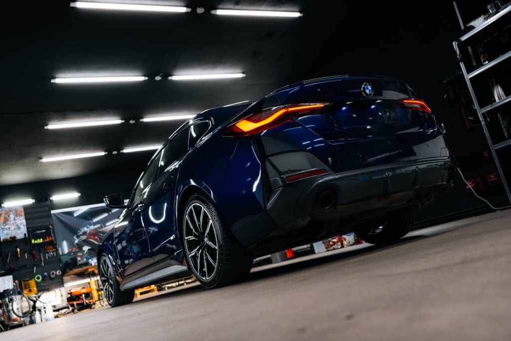 BMW detailing : Sublime bleu nuit en garage, feux LED BMW bleu nuit brillant, vue de l'arrière gauche dans un garage. Feux arrière LED allumés, logo BMW. Pneus Michelin Pilot Sport S sur jantes multi-branches.